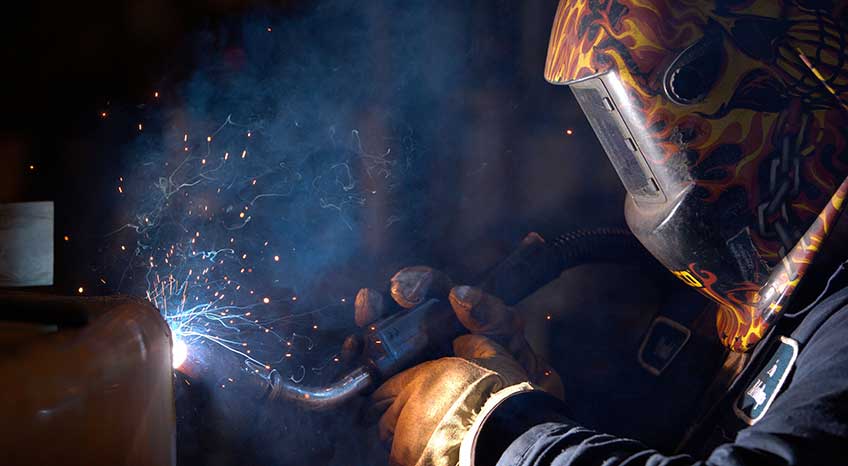 Wearing a large facemask, a manufacturer welds metal together
